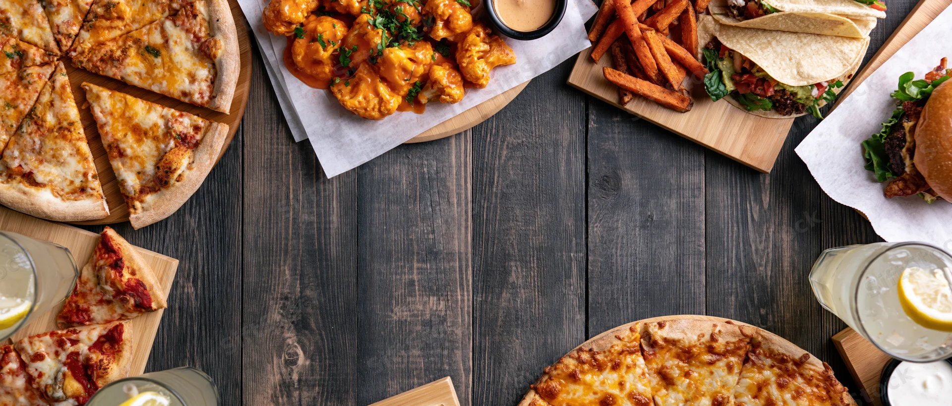 Assorted restaurant food arranged in flat lay on dark wooden table with copyspace in center