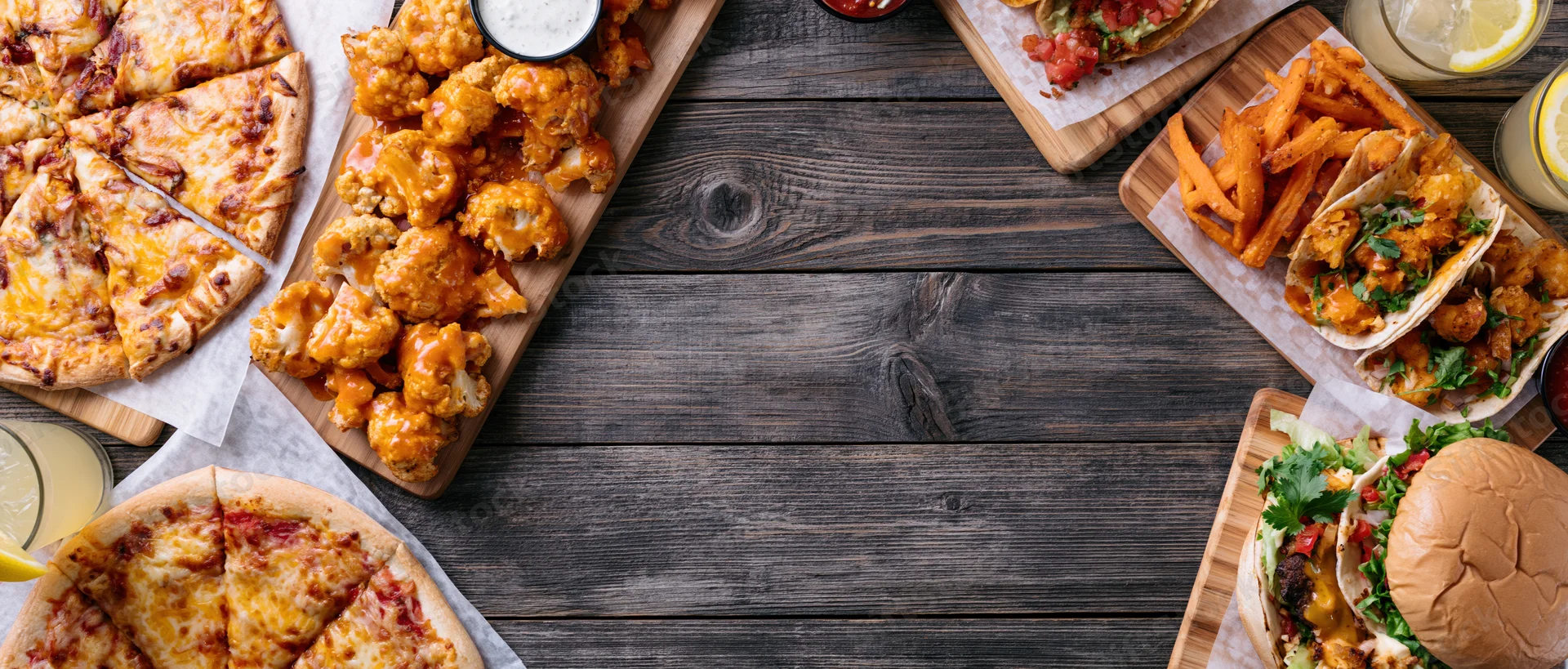 Assorted restaurant food arranged on wooden table with central copyspace