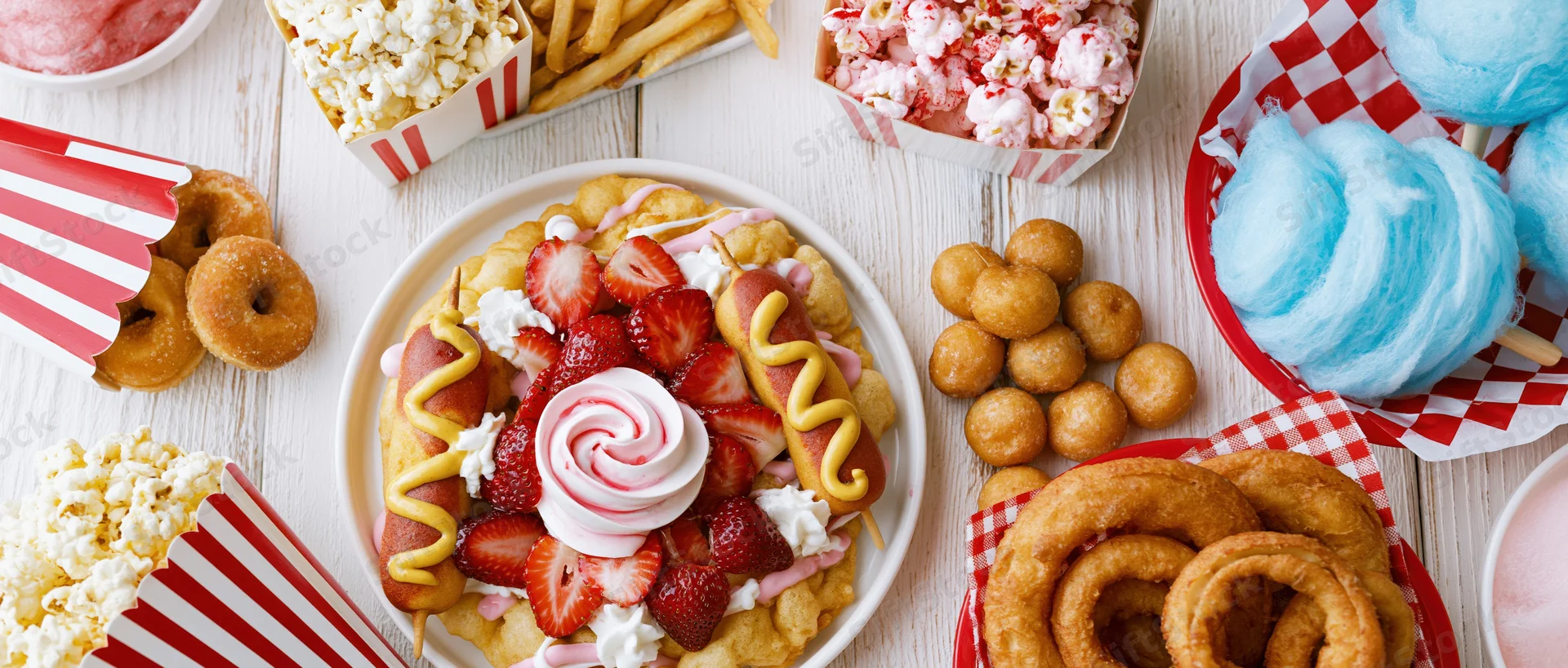 Overhead flat lay of classic american state fair foods spread on a white wooden surface