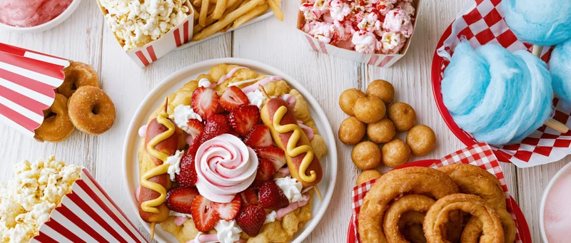 Overhead flat lay of classic american state fair foods spread on a white wooden surface