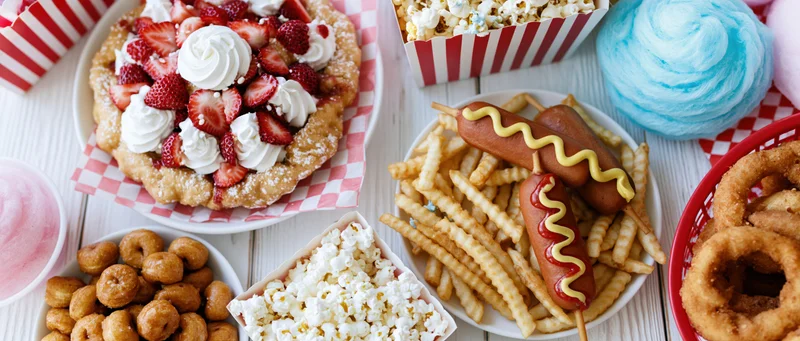 Overhead flat lay of classic american state fair foods spread on a white wooden surface