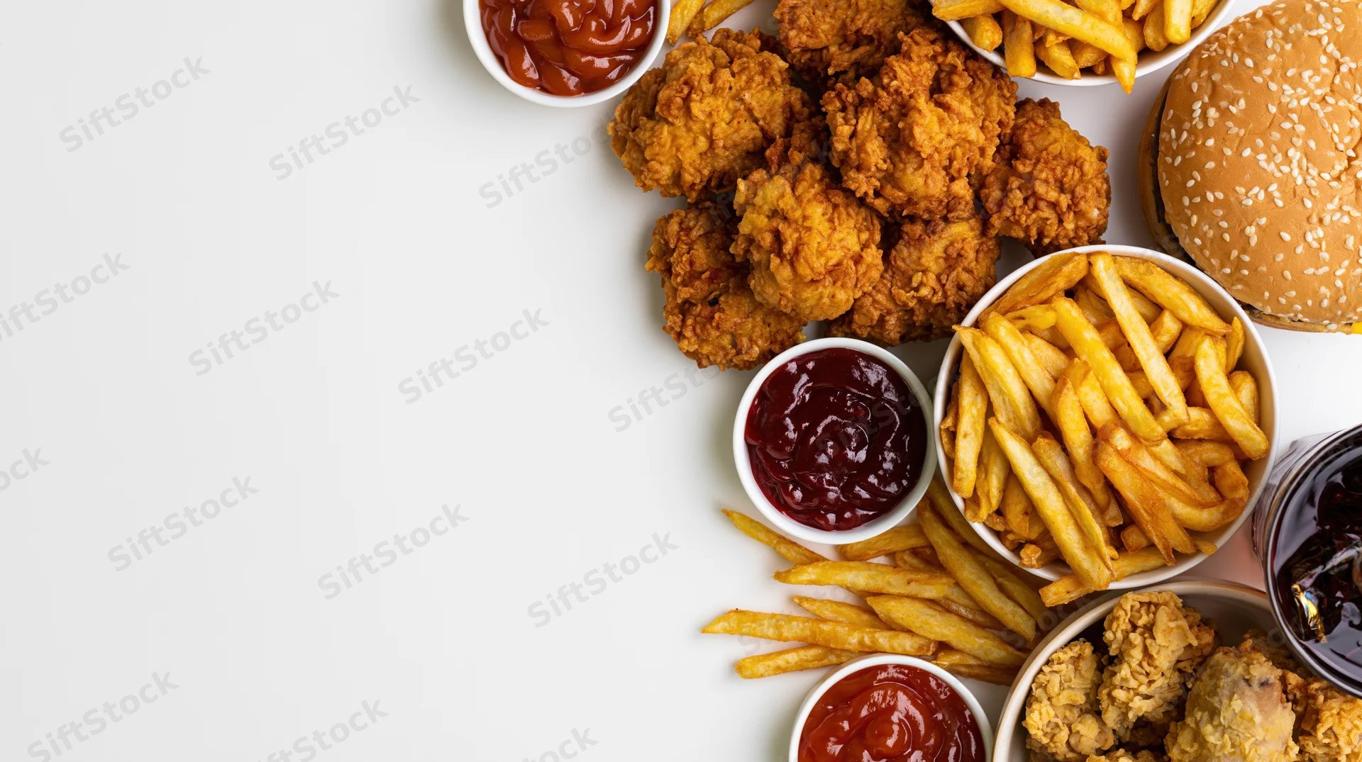 Fast food spread with fried chicken, fries, burger and sauces arranged along the right side on white surface
