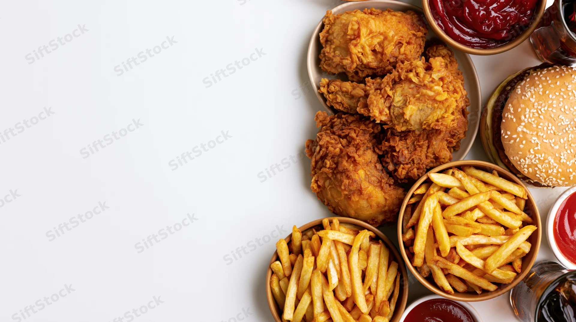 Fast food spread with fried chicken, fries, burger and condiments arranged on white surface in overhead flat lay