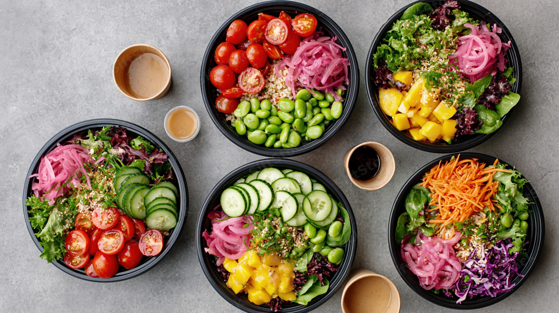 Five black takeout bowls filled with colorful salads arranged on a gray countertop