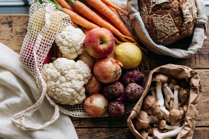 Fresh vegetables and bread arranged in mesh and paper bags on a wooden board