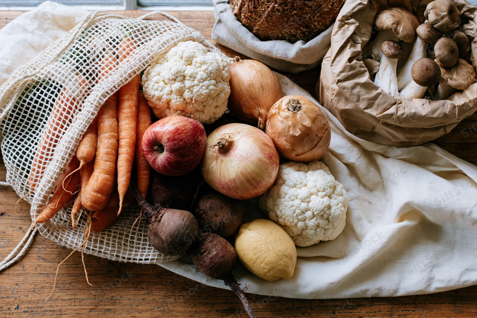Fresh vegetables and bread arranged in mesh and paper bags on wooden table
