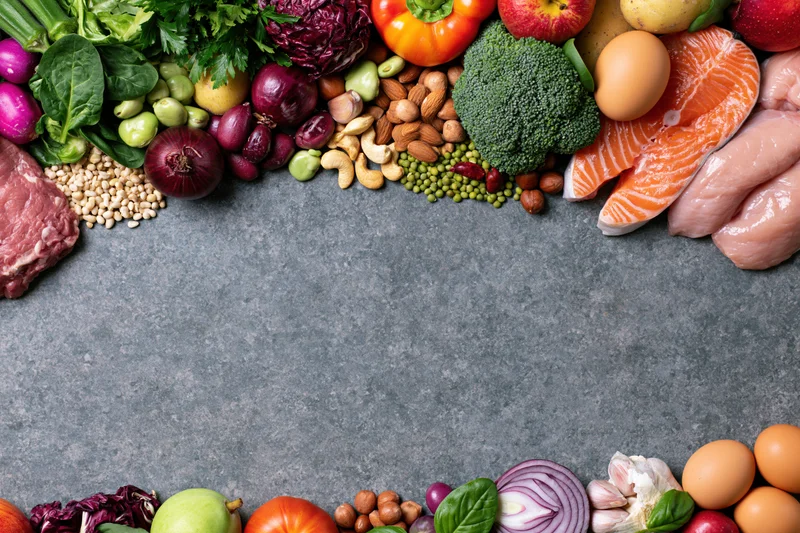 Fresh whole foods arranged in a border around a gray stone surface with copyspace in center