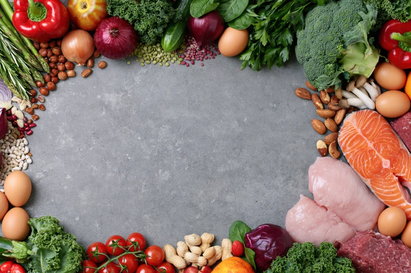 Fresh whole foods arranged in a frame around a gray surface with copyspace in center