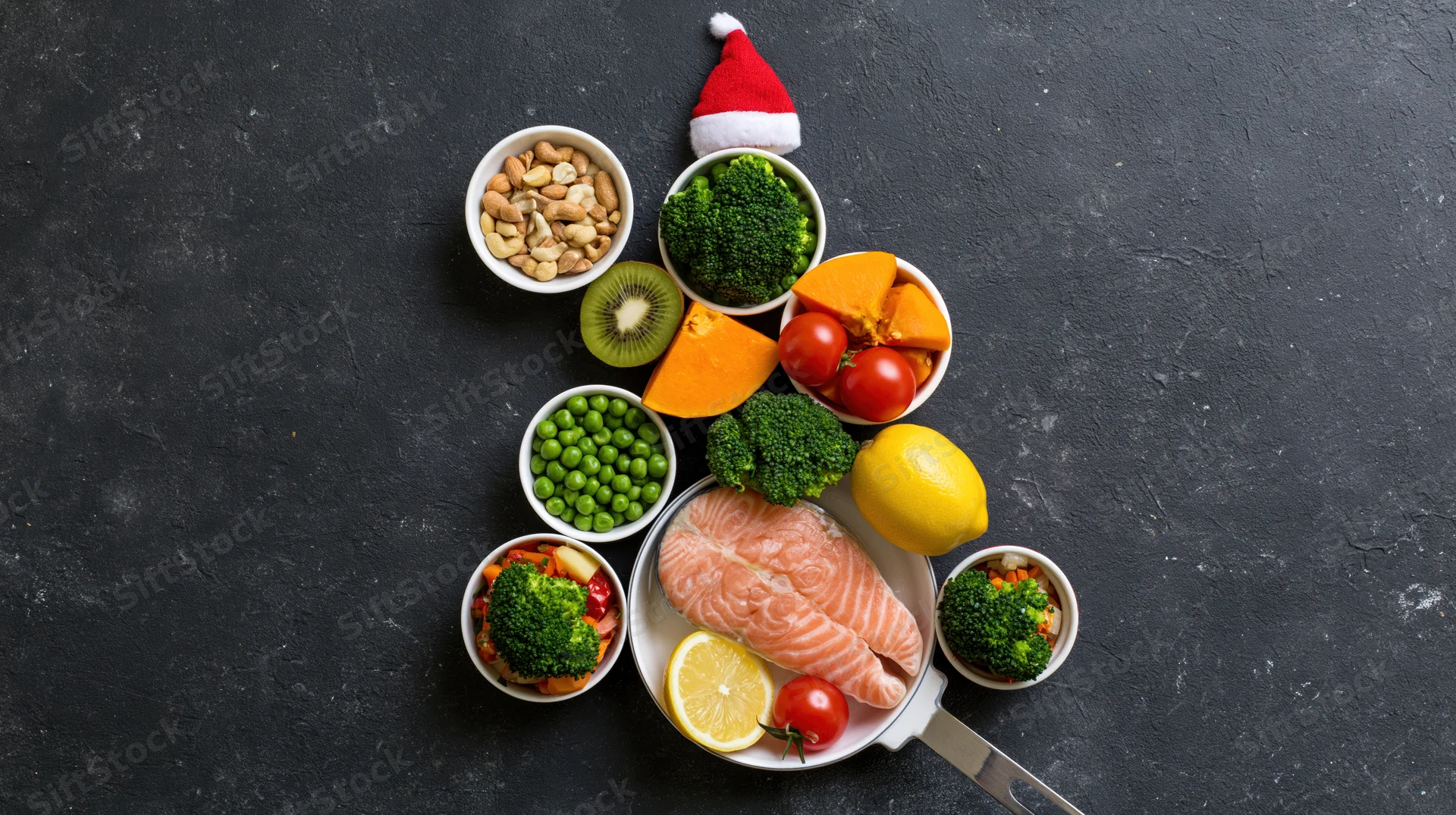 Healthy foods arranged in christmas tree shape on dark surface with santa hat on top