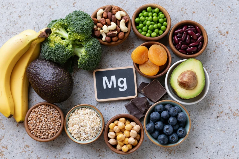 Magnesium-rich foods arranged in bowls and clusters on a gray stone surface in overhead flat lay view