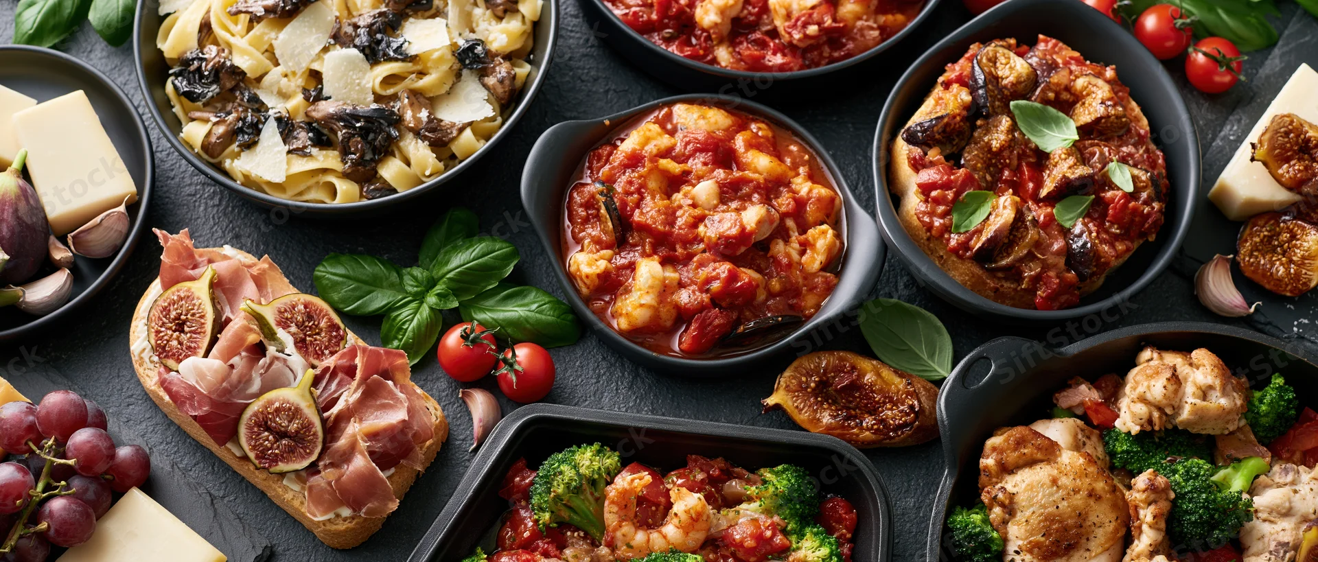 Overhead flat lay of multiple italian dishes arranged on dark surface with fresh herbs and ingredients