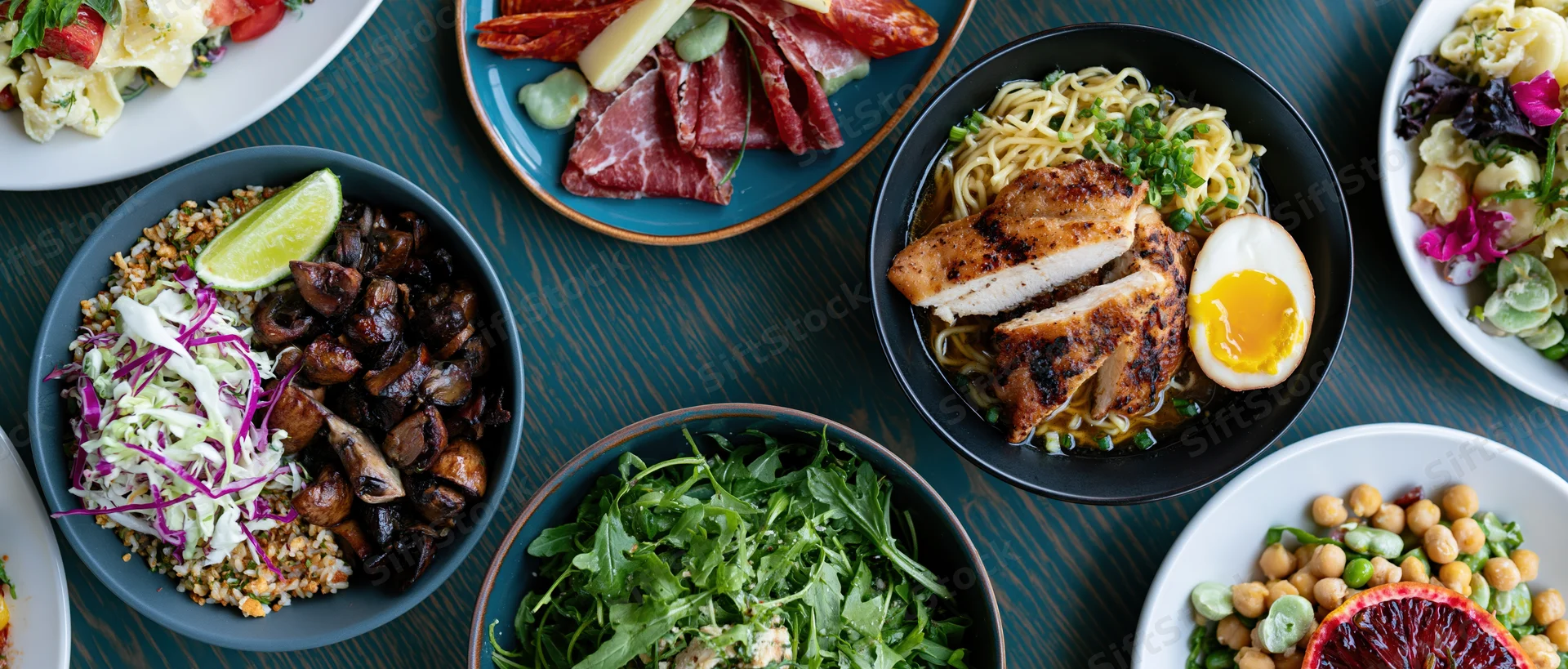 Overhead view of multiple dishes including pasta, salad, and charcuterie arranged on a dark wooden table