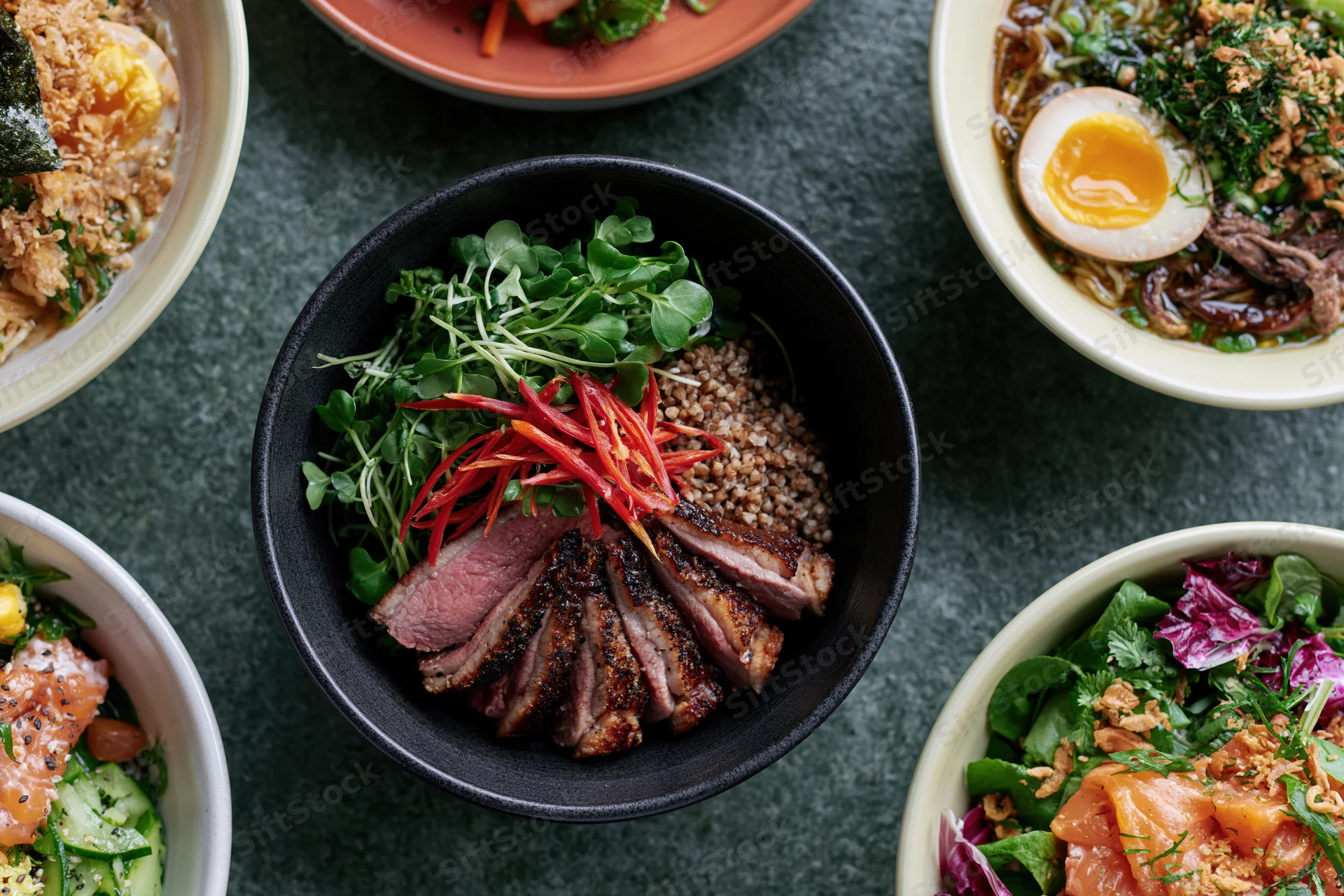 Overhead view of multiple bowls of asian fusion dishes arranged on a dark surface
