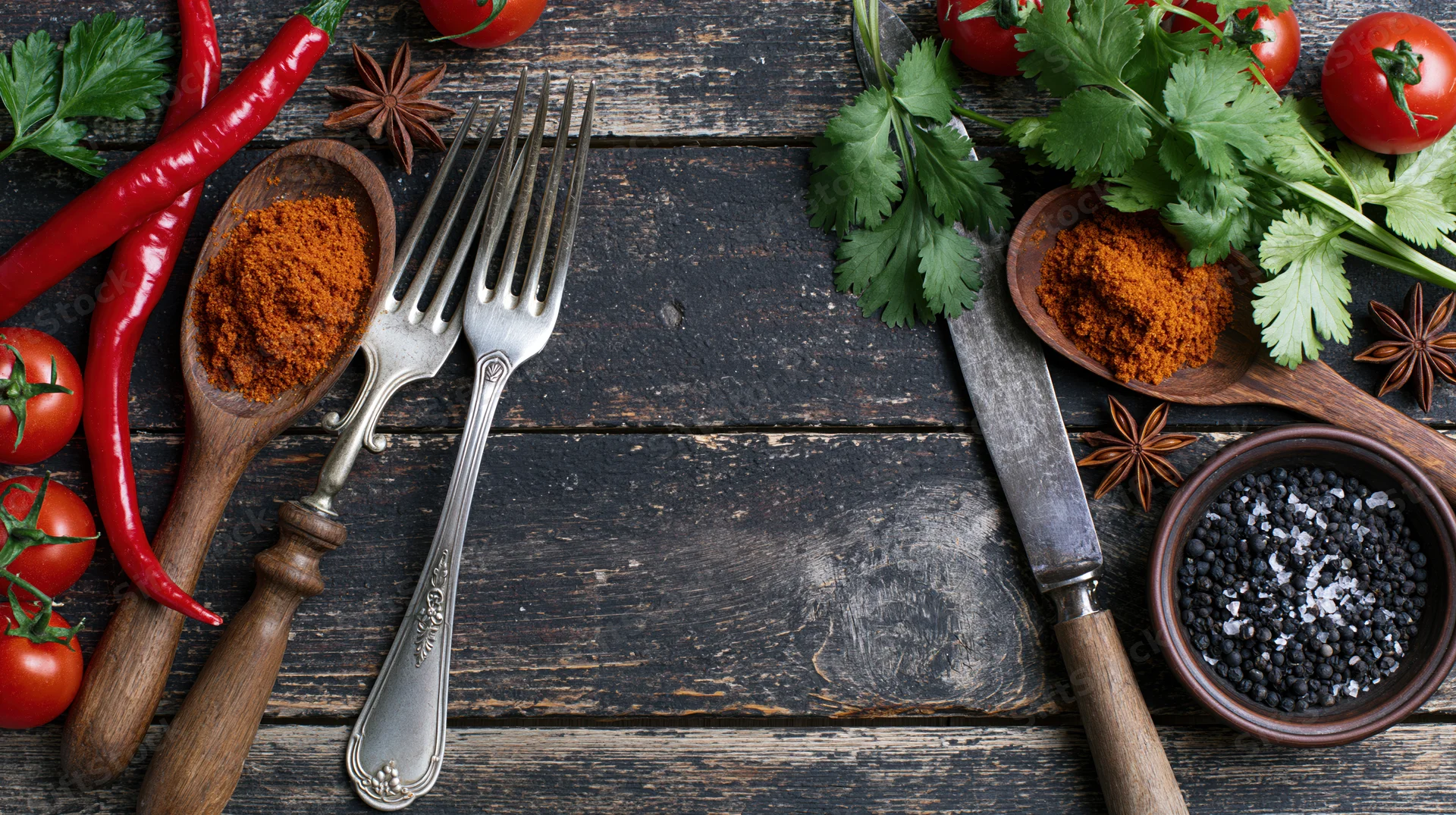 Overhead flat lay of spices, herbs, and vintage silverware arranged on dark wooden table