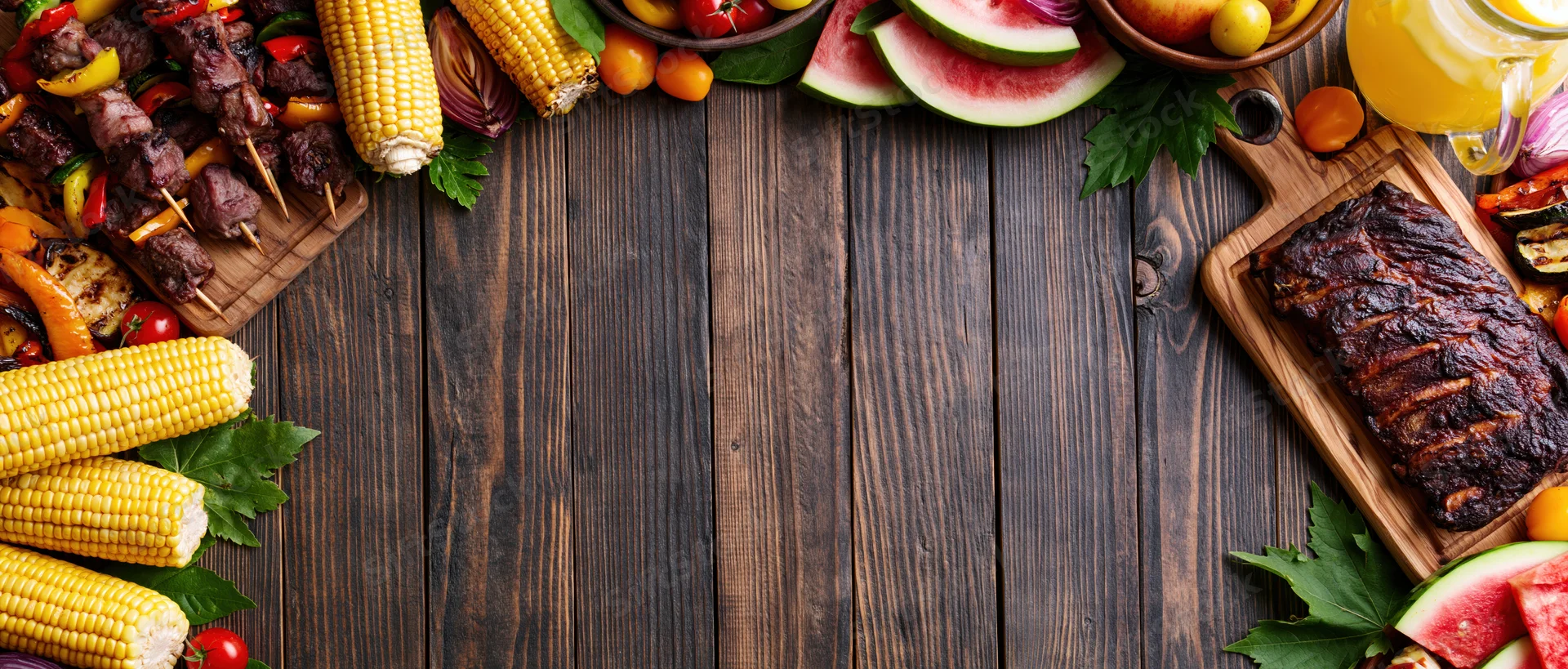 Summer barbecue spread arranged as border on dark wooden table with copyspace in center