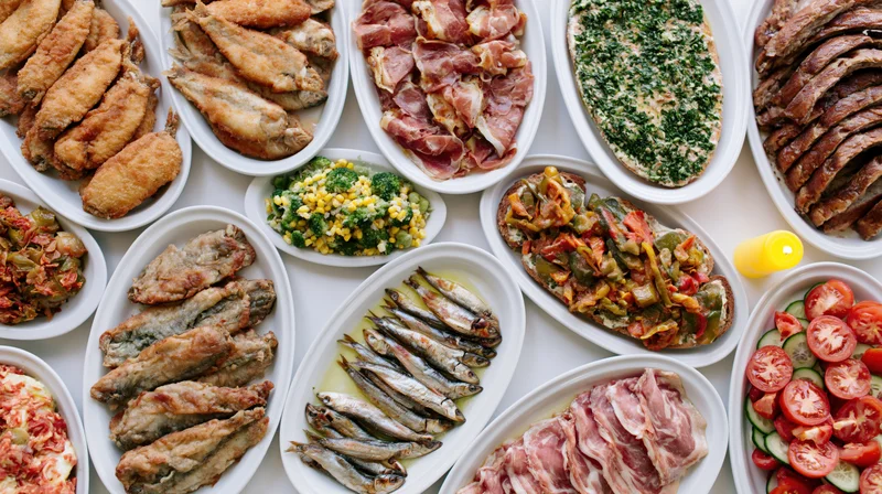 Overhead view of a festive buffet table filled with various dishes including meats, fish, vegetables, and bread arranged on white platters