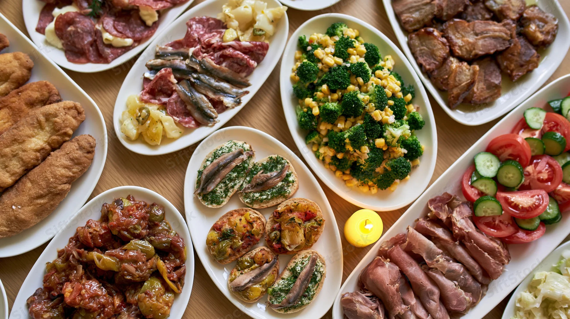 Overhead view of a festive buffet table with assorted meats, vegetables, and appetizers arranged on white platters