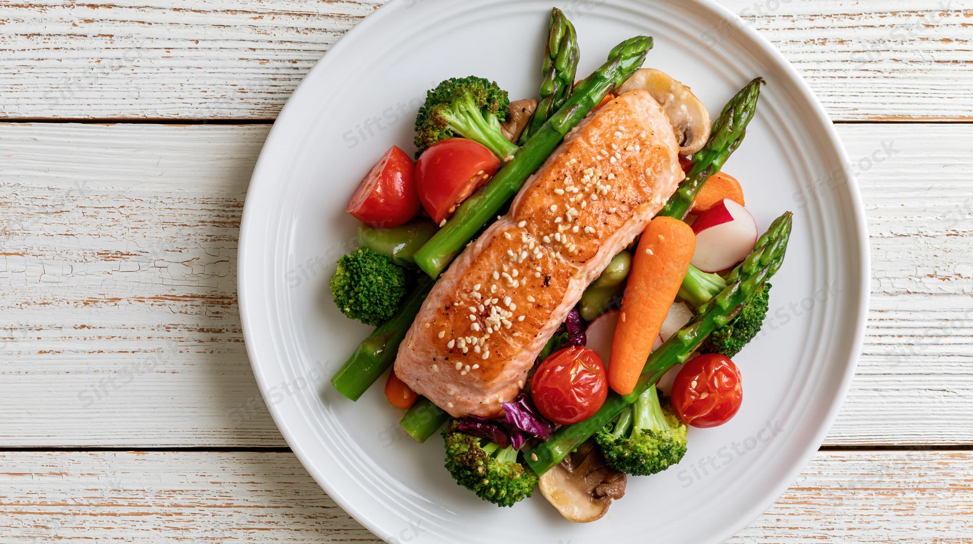 Pan-seared salmon fillet with sesame seeds served on a bed of vegetables on a white plate atop a wooden table