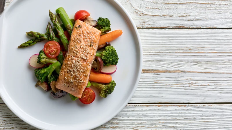 Pan-seared salmon fillet topped with sesame seeds on a bed of vegetables served on a white plate on a wooden table