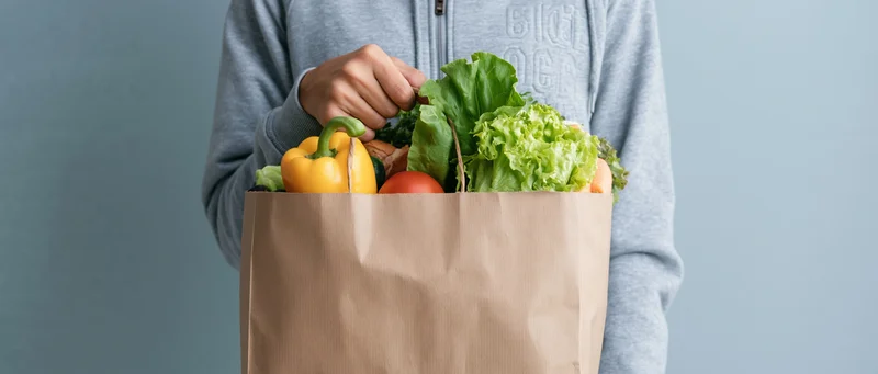 Person holding a brown paper bag filled with fresh vegetables and produce