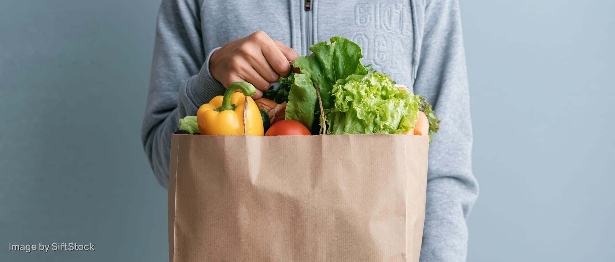 Person holding a brown paper bag filled with fresh vegetables and produce