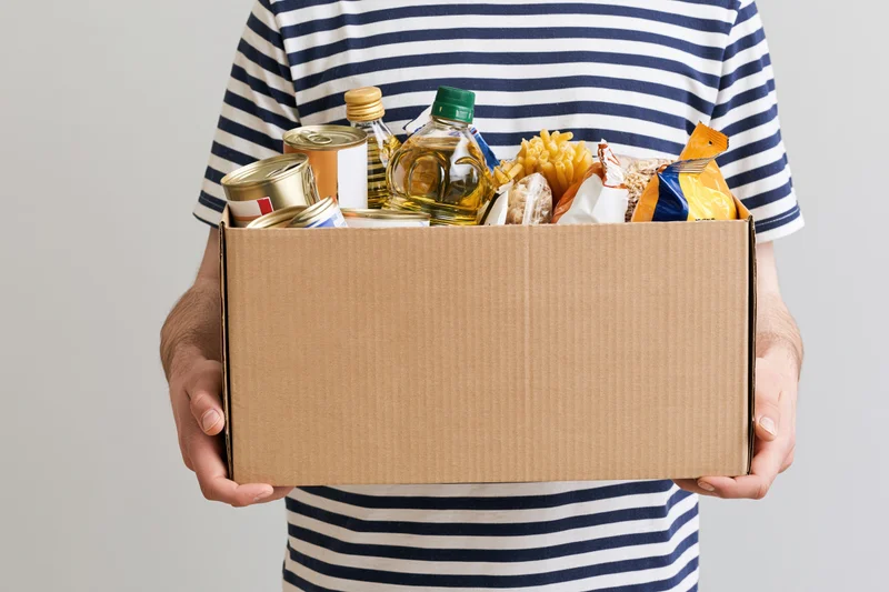 Man holding a cardboard box filled with canned goods and packaged food for donation
