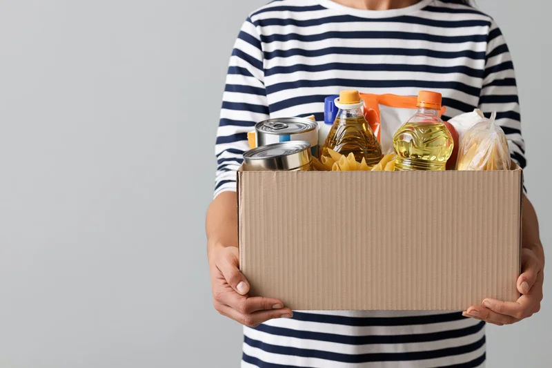 Woman holding a cardboard box filled with canned goods and cooking supplies