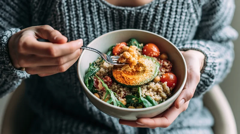 Woman holding a ceramic bowl of quinoa salad with avocado and tomatoes, eating with a fork