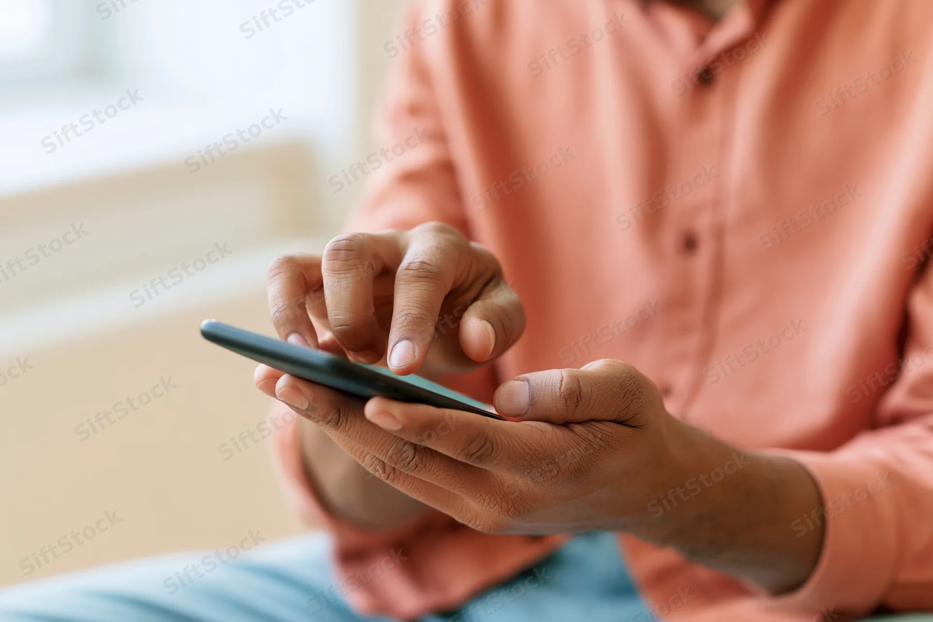 Man tapping smartphone screen with one finger while holding device in both hands indoors