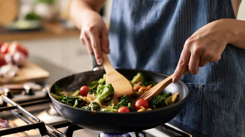 Woman stirring vegetables in a wok on a gas stove in a kitchen