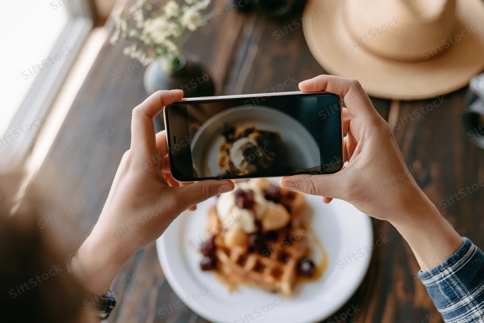 Hands holding smartphone horizontally photographing waffle dessert on wooden table