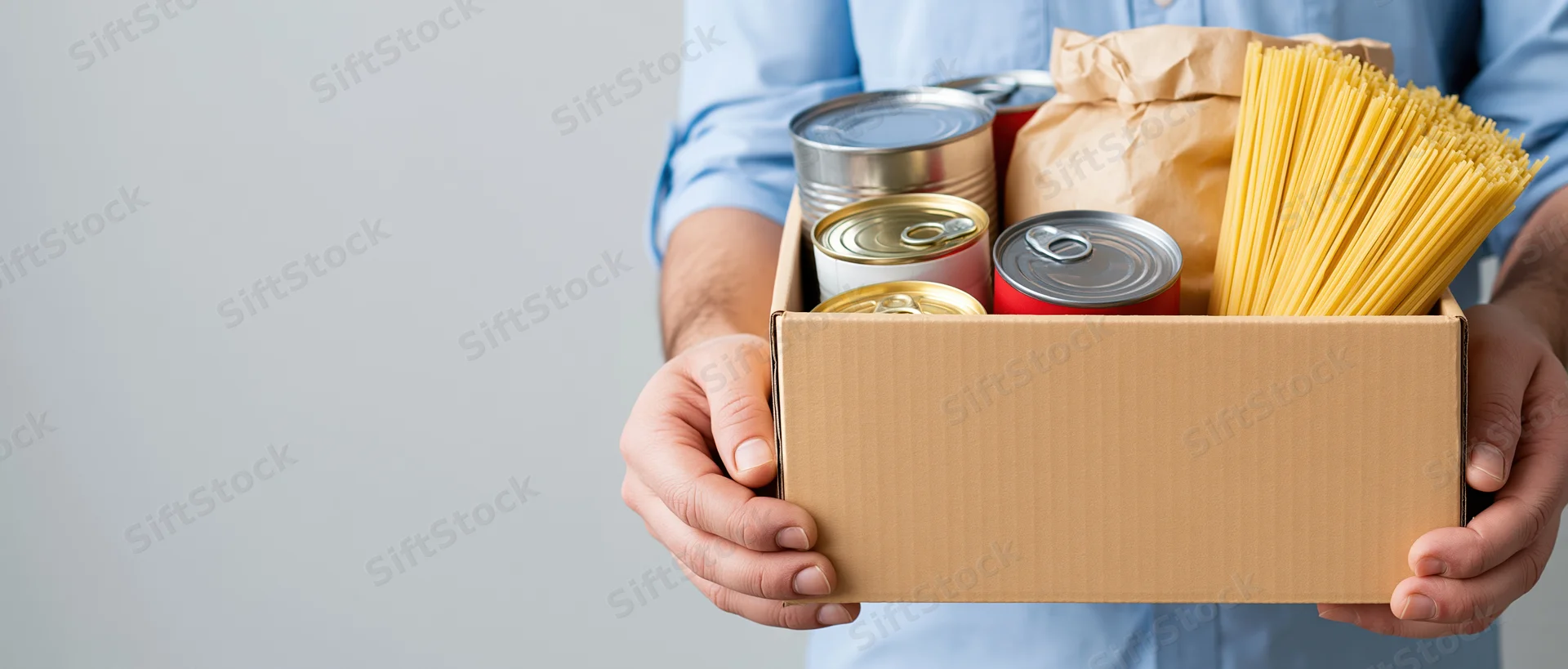 Man holding a cardboard box filled with canned goods and pasta for donation