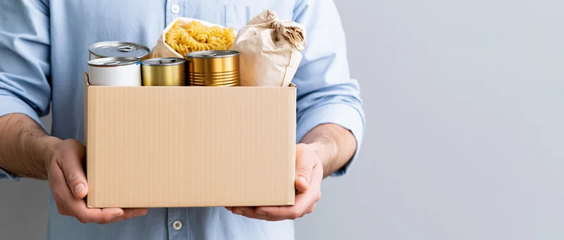 Man holding a cardboard box filled with canned food and pasta for donation