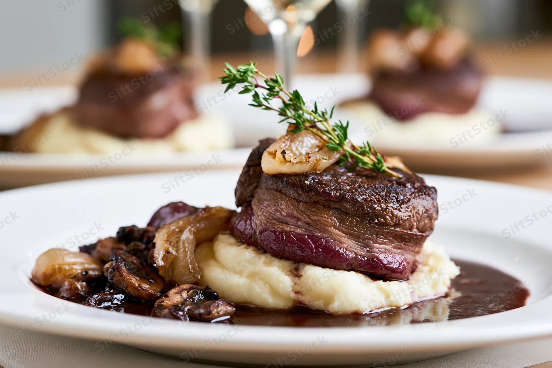 Beef medallion wrapped in bacon served on mashed potatoes with gravy and herbs on a white plate