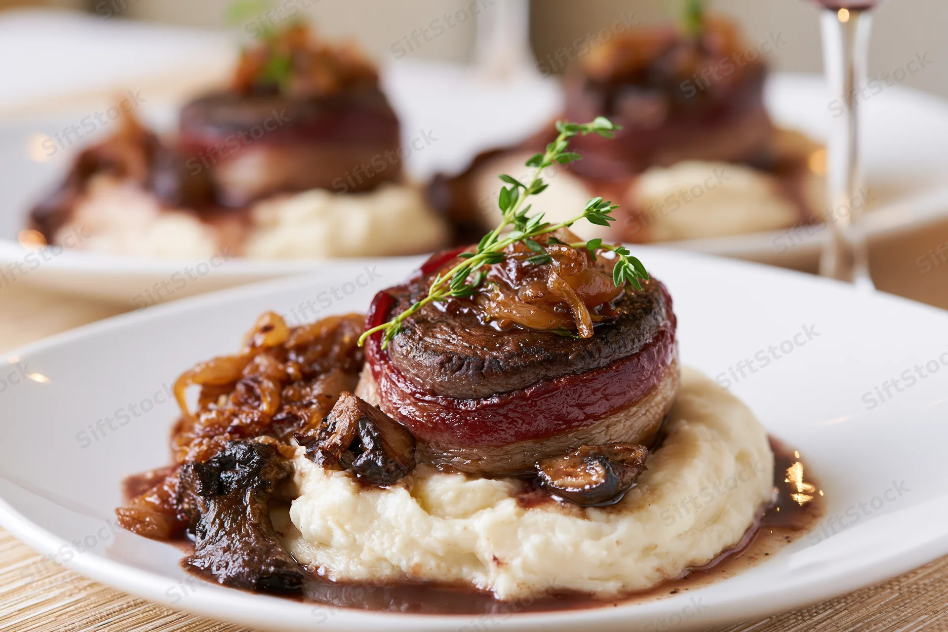 Bacon-wrapped beef medallion on mashed potato with gravy and thyme garnish on white plate
