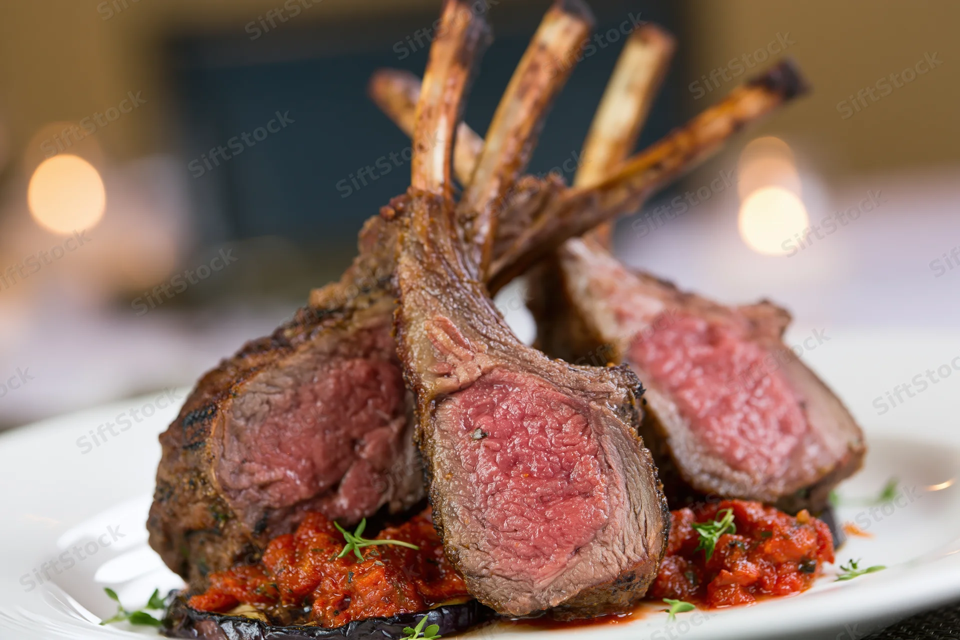 Grilled rack of lamb chops with tomato sauce and herbs on a white plate in a restaurant setting