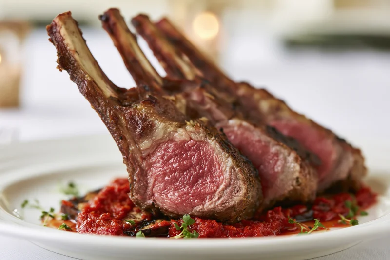 Grilled rack of lamb chops served on a white plate with tomato sauce and herbs in a restaurant setting