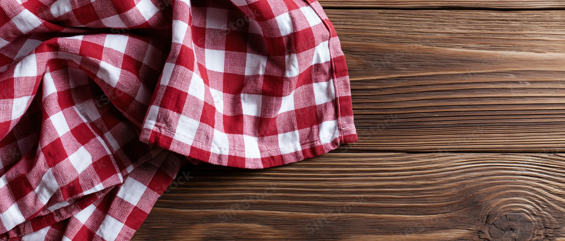 Red and white gingham cloth napkin casually draped on a wooden table surface