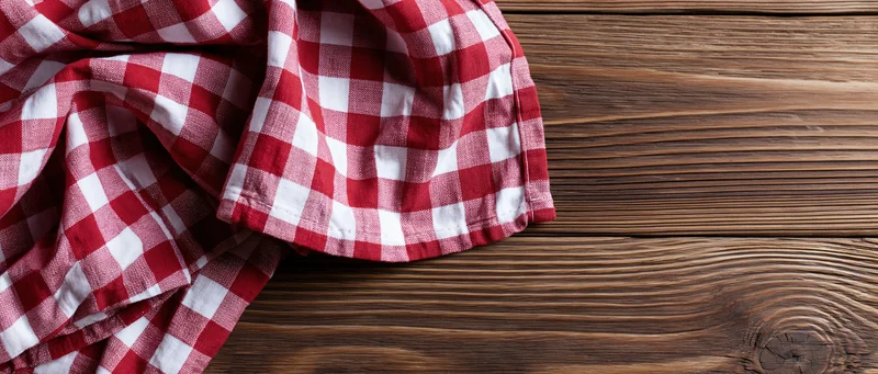 Red and white gingham cloth napkin casually draped on a wooden table surface