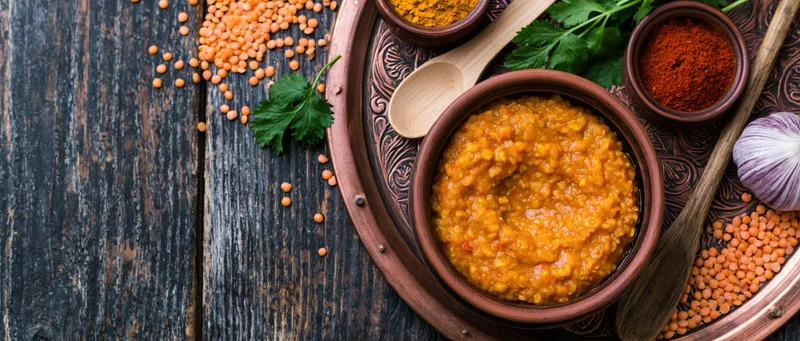Red lentil dal in a clay bowl on an engraved copper tray with spices and herbs on a dark wooden table
