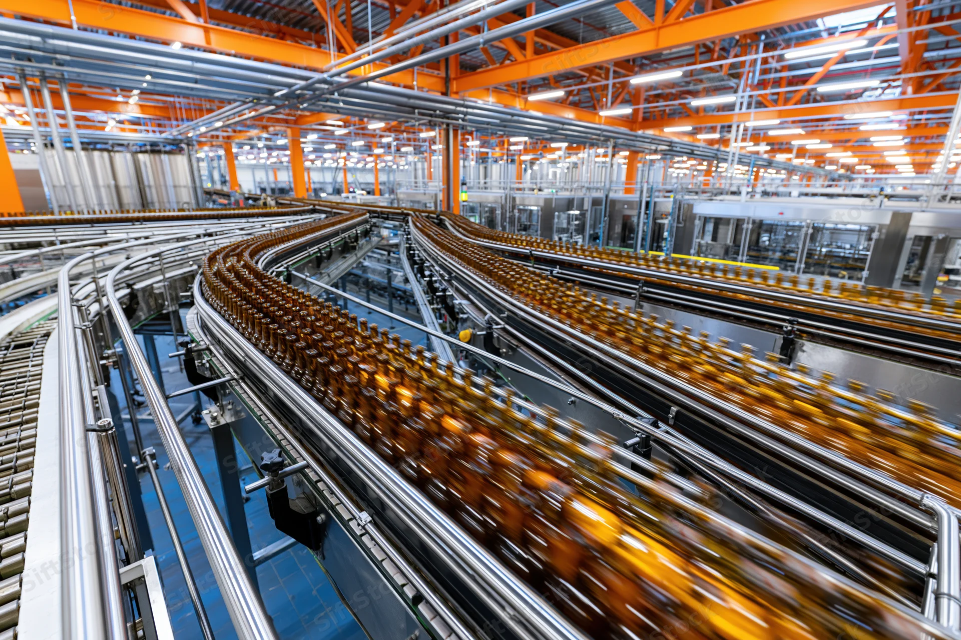 Amber glass bottles moving along converging conveyor belts in a factory production line