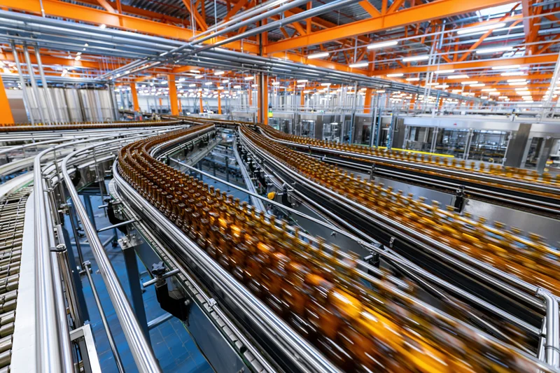 Amber glass bottles moving along converging conveyor belts in a factory production line