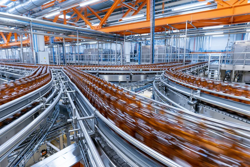 Amber glass bottles moving along converging conveyor belts in a factory production line