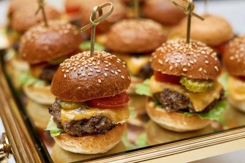 Mini beef sliders with cheese and vegetables arranged on a mirrored catering tray