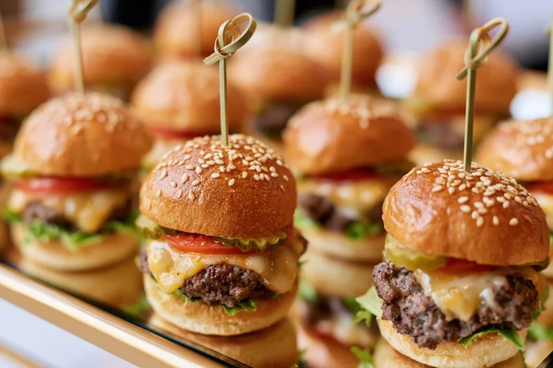 Mini beef sliders with cheese and vegetables arranged on a mirrored catering tray