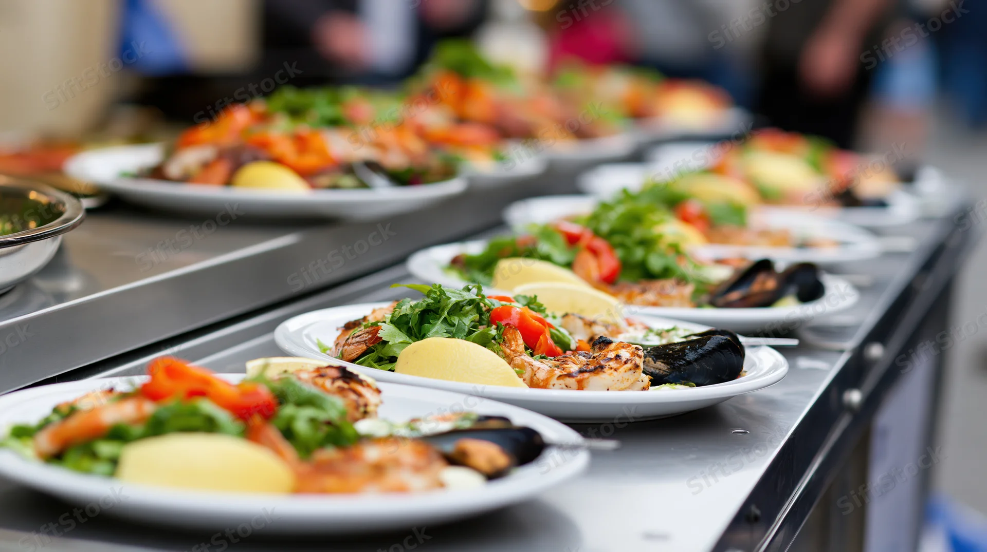 Rows of white plates with grilled seafood and garnishes arranged on a metal buffet counter