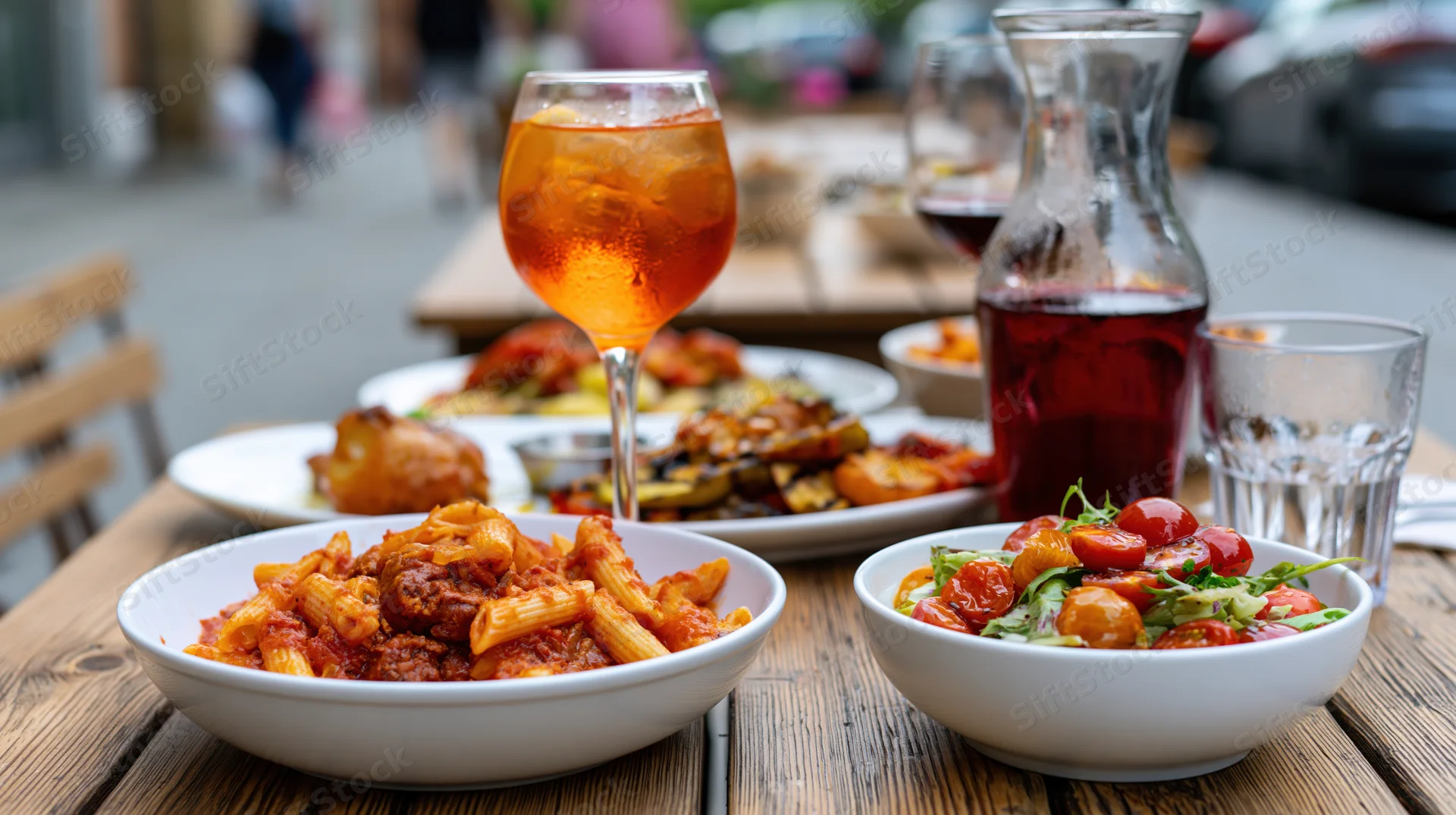 Rustic wooden outdoor table set with pasta, salad, and drinks at a restaurant