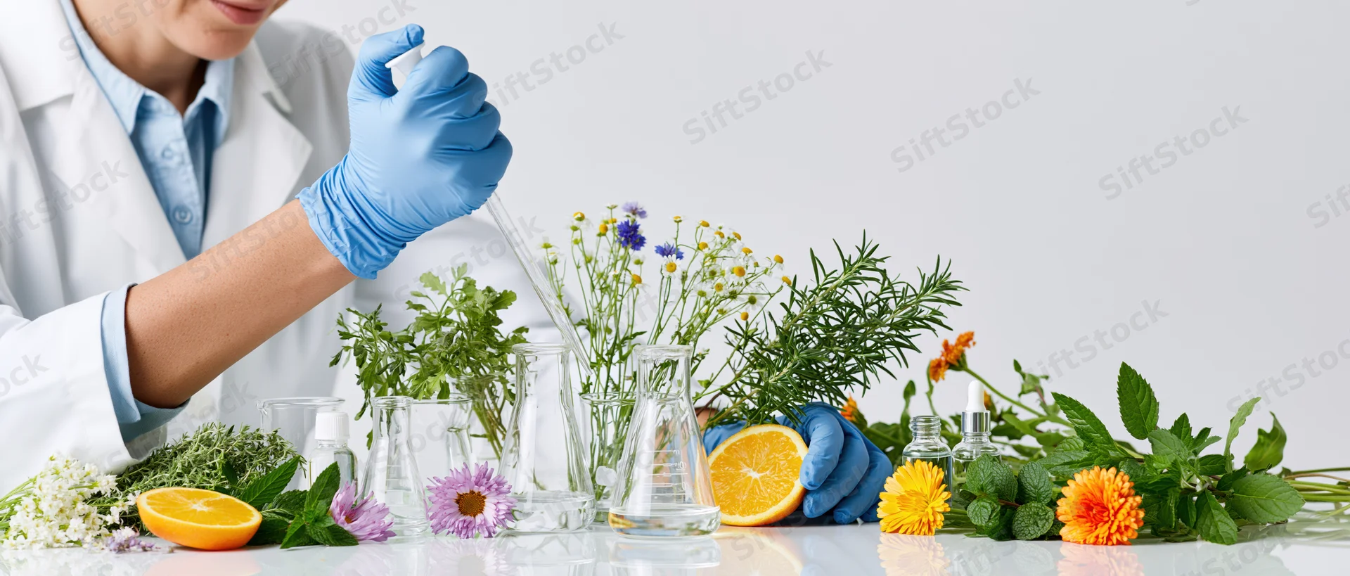Scientist using pipette to transfer liquid into beaker surrounded by herbs and flowers on lab table