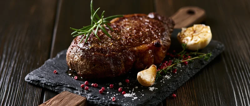 Seared beef steak on dark slate board with rosemary and garlic garnish