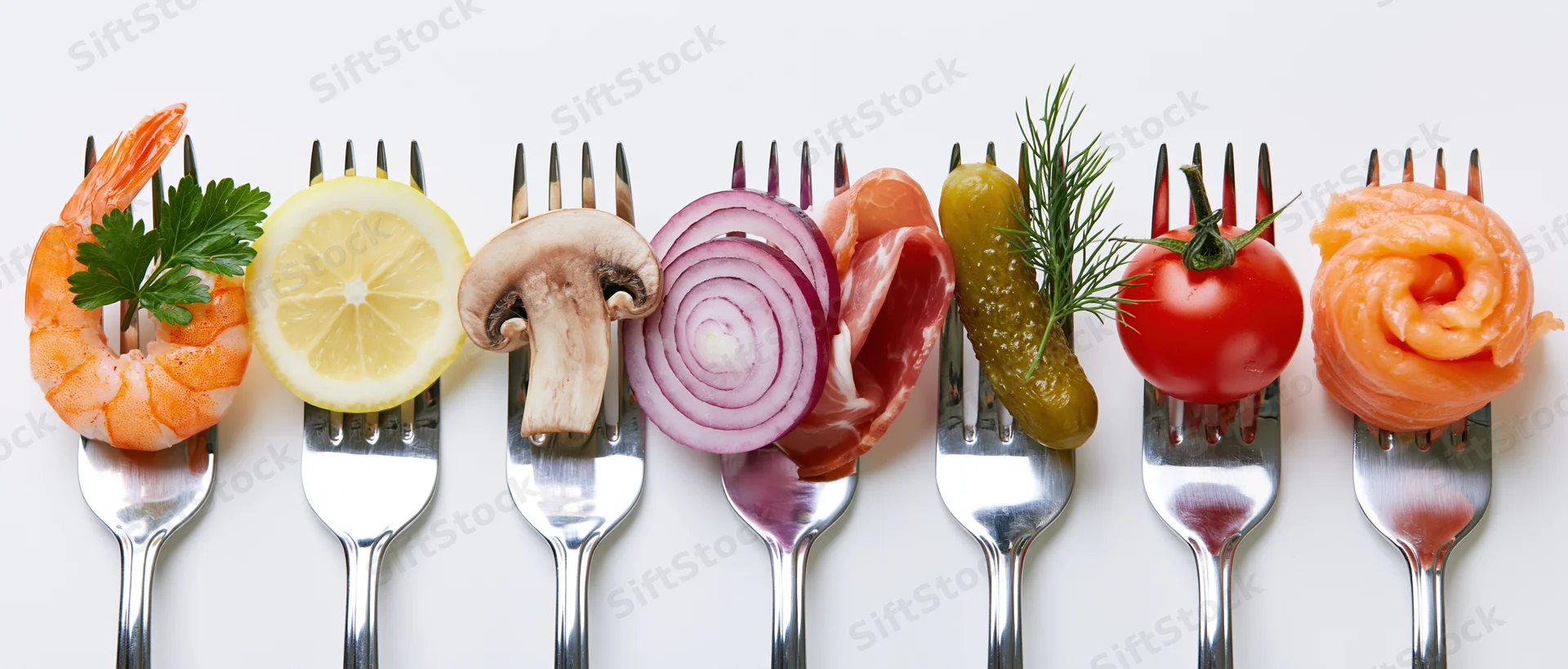 Seven forks each holding a different food item arranged in a row on a white surface